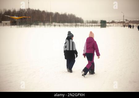 Children walk through snowy field. Children walk outside in winter. Warm clothes in cold weather. Walk down street. Stock Photo