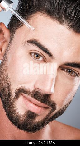 Beauty, oil and man with pipette for skincare, self care and treatment to glow or smooth skin isolated in a studio gray background. Portrait, face and Stock Photo