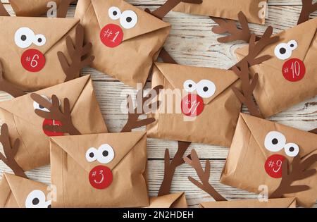 Set of gifts in envelopes with deer faces on white wooden table, flat lay. Christmas advent calendar Stock Photo