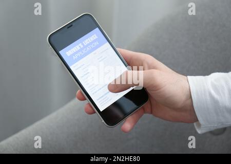 Man holding smartphone with driver's license application form at home, closeup Stock Photo