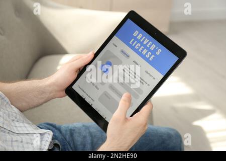 Man holding tablet with driver's license application form at home, closeup Stock Photo