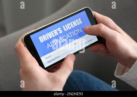 Man holding smartphone with driver's license application form at home, closeup Stock Photo