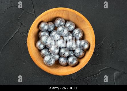 Hazelnut candies in chocolate in a wooden bowl on a dark concrete background, top view. Stock Photo