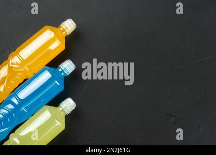 Three plastic bottles with lemon, orange and blue isotonic drinks on a dark concrete background. copy space. Stock Photo