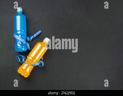 Plastic bottles with yellow and blue isotonic for drinking wrapped with a measuring tape on a dark concrete background. copy space. Stock Photo