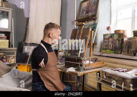 a young man with disabilities paints a picture with oil paints in an art workshop Stock Photo