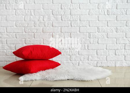 Stylish red pillows on floor near light brick wall Stock Photo