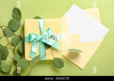 Envelope with blank card, gift box and eucalyptus branches on green background. Hello spring Stock Photo