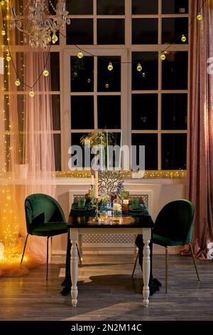 Romantic dinner table setting for couple with festive lights, Table for a celebration or wedding reception. Evening time, golden and green colors, dar Stock Photo
