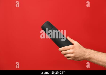 Man holding black thermos on red background, closeup Stock Photo