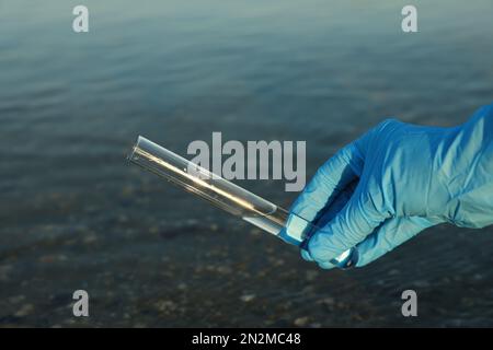 Scientist with test tube taking sample from river for analysis, closeup Stock Photo