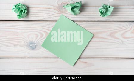 Flat lay of blank empty green sticker sticky note near crumpled notes on grey wooden table. Search, no idea, creative work, brainstorming, lack of Stock Photo