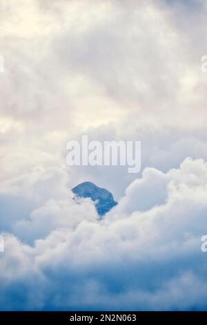 mountaintop peeking through fluffy cumulus clouds after sunset Stock Photo