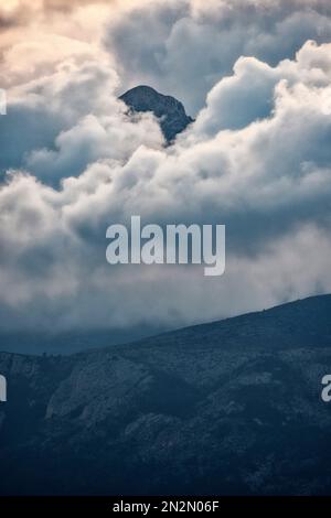 mountaintop peeking through fluffy cumulus clouds after sunset Stock Photo