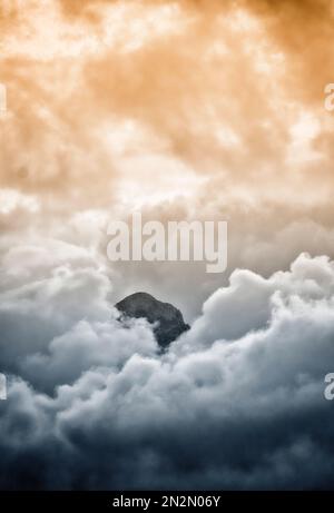 mountaintop peeking through fluffy cumulus clouds after sunset Stock Photo