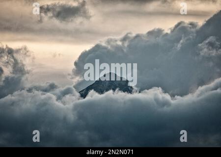 mountaintop peeking through fluffy cumulus clouds after sunset Stock Photo