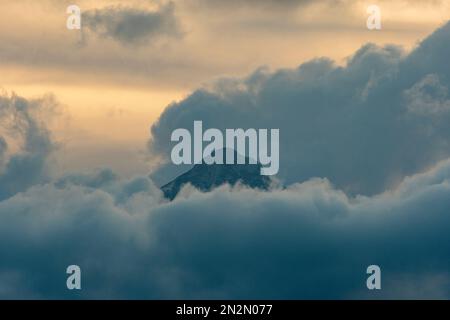 mountaintop peeking through fluffy cumulus clouds after sunset Stock Photo