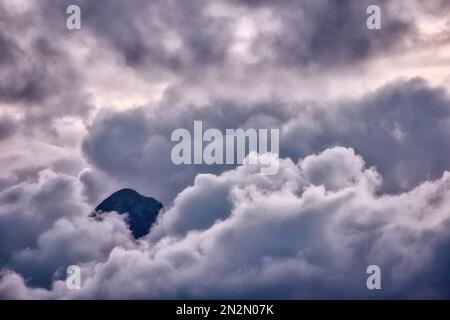 mountaintop peeking through fluffy cumulus clouds after sunset Stock Photo