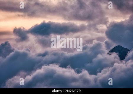 mountaintop peeking through fluffy cumulus clouds after sunset Stock Photo