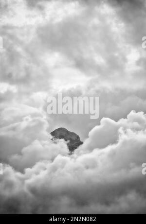 mountaintop peeking through fluffy cumulus clouds after sunset in black and white Stock Photo