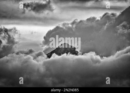 mountaintop peeking through fluffy cumulus clouds after sunset in black and white Stock Photo