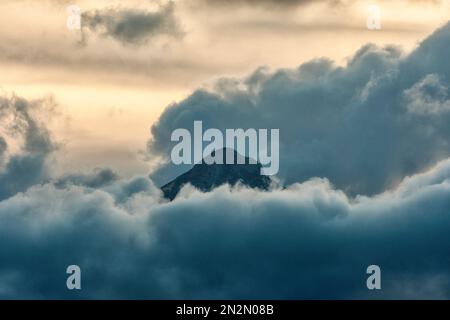 mountaintop peeking through fluffy cumulus clouds after sunset Stock Photo