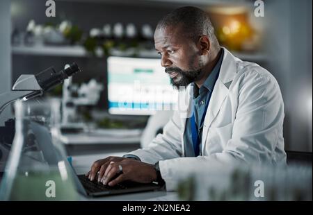 Scientist man, laptop and doing research in a laboratory with information technology and data analytics. Black person or doctor typing online at night Stock Photo