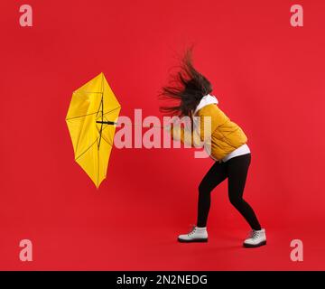 Woman with umbrella caught in gust of wind on red background Stock Photo