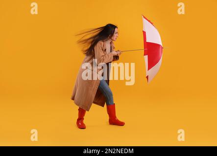 Woman with umbrella caught in gust of wind on yellow background Stock Photo