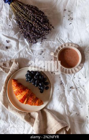 breakfast of croissant, grapes and hot chocolate, morning scene on the bed, top view Stock Photo