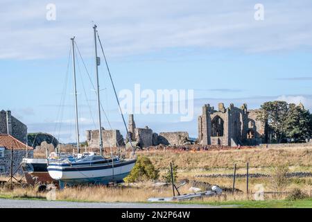 Lindisfarne, Northumberland, UK, Summer view of the ruins of the medieval Lindisfarne Priory with boats in the foreground. No people. Copy Space. Stock Photo