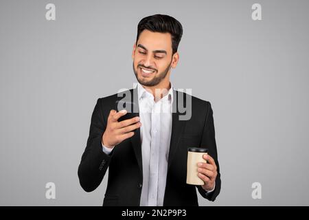 Hamdsome Young Arab Businessman Using Smartphone And Holding Takeaway Coffee Stock Photo
