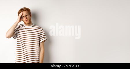 Tired young man student touching head, looking complex and tired, standing over white background Stock Photo