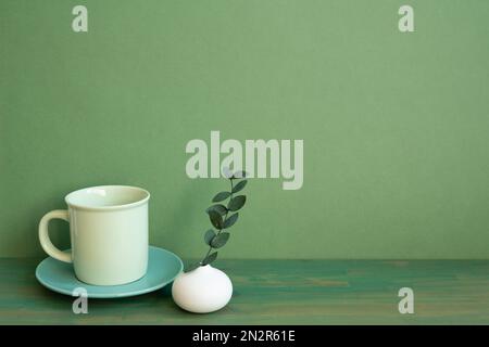Coffee cup and eucalyptus leaf on wooden table. green wall background. minimal, copy space Stock Photo