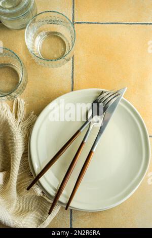 Overhead view of plates and cutlery on a  tiled table next to glasses, table runner and a jug of water Stock Photo