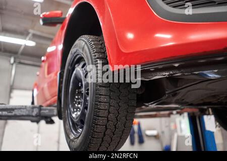 Red car on an elevator or hoist in a repair workshop or garage with ...