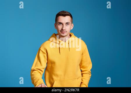 positive handsome man in yellow sweatshirt on blue Stock Photo