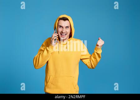 angry man in yellow sweatshirt holding mobile phone Stock Photo