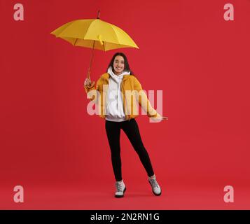 Woman with umbrella caught in gust of wind on red background Stock Photo