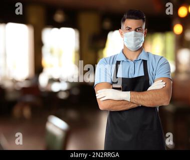 Waiter in medical face mask in restaurant. Space for text Stock Photo