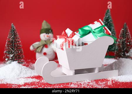 Sleigh with gift boxes and Christmas decorations on red background Stock Photo