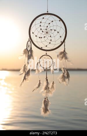 Beautiful handmade dream catcher near river at sunset. Space for text  Photos