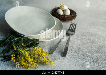 Close-up of an Easter place setting with yellow mimosa flowers and a bird's nest with eggs Stock Photo