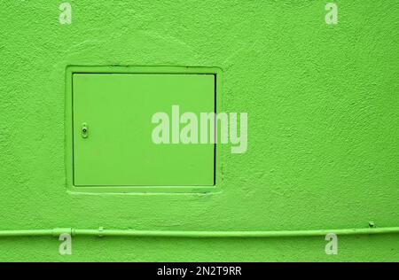 Closed inspection hatch located over pipe on plaster wall of bright green building Stock Photo