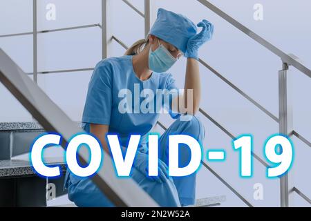 Tired overwhelmed nurse sitting on stairs in hospital. Medical system collapse during coronavirus pandemic Stock Photo