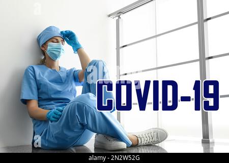 Tired overwhelmed nurse sitting on floor in hospital. Medical system collapse during coronavirus pandemic Stock Photo