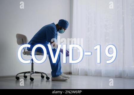 Tired overwhelmed doctor sitting on chair in hospital. Medical system collapse during coronavirus pandemic Stock Photo