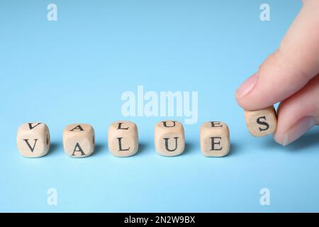 Woman making word VALUES with beads on light blue background, closeup Stock Photo