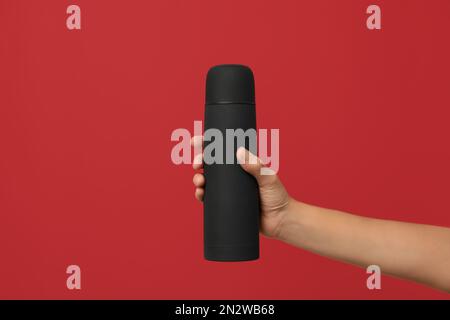 Woman holding modern black thermos on red background, closeup Stock Photo