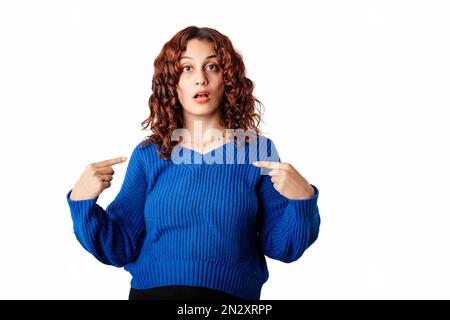 Portrait of young woman wearing blue knitted sweater standing isolated over white background pointing at herself, shocked and cheerful, self-promoting Stock Photo